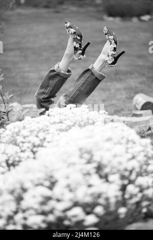 Schwarz-weißes Bild einer weiblichen Beine in Jeans und High Heels in einem Park Stockfoto