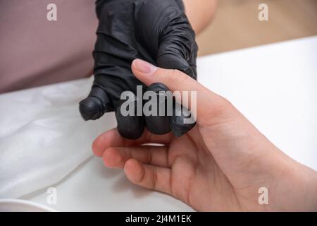 Nahaufnahme von schönen Frauenhänden, die im Spa-Salon Maniküre bekommen. Weibliche Manikuristin, die die Nagelhaut mit einem professionellen Maniküre-Stopfer reinigt. Kosmetische PR Stockfoto