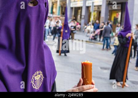 Die brennende Kerze eines jungen Nazareners mit einem Rosenkranz zum Beten in ihren Händen, während er seine Buße in der Karwoche-Prozession tat. Stockfoto