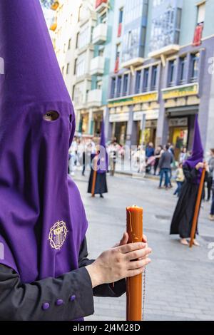 Die brennende Kerze eines jungen Nazareners mit einem Rosenkranz zum Beten in ihren Händen, während er seine Buße in der Karwoche-Prozession tat. Stockfoto