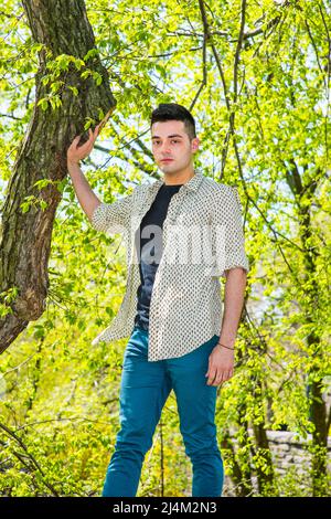 Ein junger, gutaussehender Kerl steht am Morgen einer Frühjahrssaison bei einem Baum. Stockfoto