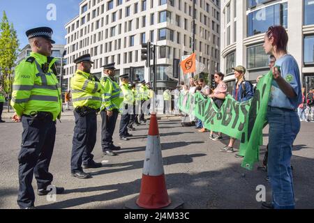 London, England, Großbritannien. 16. April 2022. Aktivisten halten ein Transparent mit der Aufschrift „Wir werden nicht umstehen“ vor einer Reihe von Polizeibeamten. Die Demonstranten des Extinction Rebellion blockierten Marble Arch mit einer Limousine. Mehrere Aktivisten befestigten sich an dem Fahrzeug, während Hunderte von Demonstranten auf der Straße saßen. Die Demonstranten fordern, dass die Regierung gegen die Klima- und Umweltkrise handelt. (Bild: © Vuk Valcic/ZUMA Press Wire) Bild: ZUMA Press, Inc./Alamy Live News Stockfoto