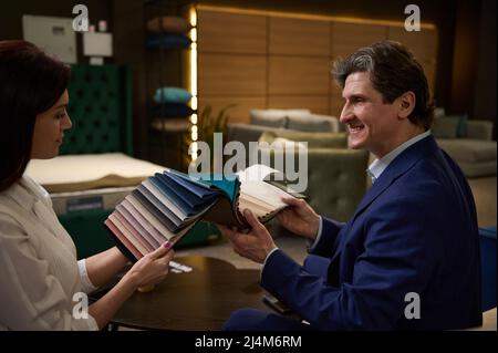 Rückansicht eines kaukasischen Paares mittleren Alters, das Farbstoffmuster hält und im Möbelgeschäft Sitzbezüge für die Couch pflückt. Stockfoto