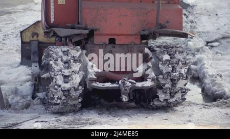 Die Rückseite einer großen technischen Maschine. CLIP. Die Räder treiben das Auto zurück durch den Schnee. Schwere Ausrüstung fährt im Schnee auf Metallgleisen Stockfoto