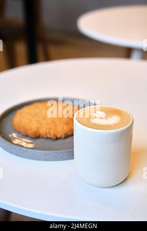 Der morgendliche Brunch im Café ist auf dem Tisch. Riesenkeks und Cappuccino mit schönem Milchschaum. Manchmal muss man in dieser schnelllebigen Welt eine Pause einlegen Stockfoto