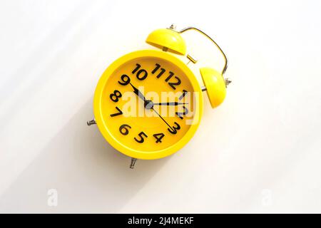 Ein gelber Retro-Wecker mit schwarzem Zifferblatt liegt schräg links auf einem weißen Tisch. Stockfoto