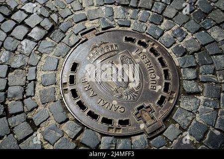Bukarest, Rumänien - 12. April 2022: Eine Kanalabdeckung mit dem Emblem von Bukarest auf einer mit Kopfsteinpflaster gepflasterten Straße im alten Zentrum. Dieses Bild ist fo Stockfoto