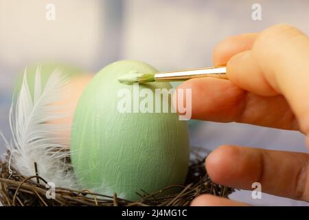 Osterei im Nest mit grünem Farbstoff bemalen. Pinsel in der Hand der Frau malen. Stockfoto