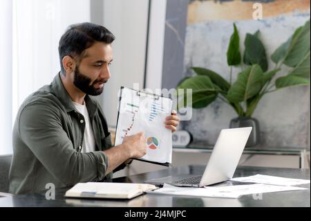 Online-Business-Briefing per Videokonferenz. Erfolgreicher indischer oder arabischer Finanzmentor oder Direktor eines Unternehmens, Durchführung eines finanziellen Brainstorms mit Kollegen, Anzeigen von Grafiken, Austausch von Informationen Stockfoto