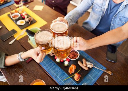 Eine Gruppe von glücklichen, unkenntlichen Freunden, die im Restaurant der Brauerei-Bar Bier trinken und toasten. Freundschaftskonzept mit jungen Menschen, die gemeinsam Spaß haben Stockfoto