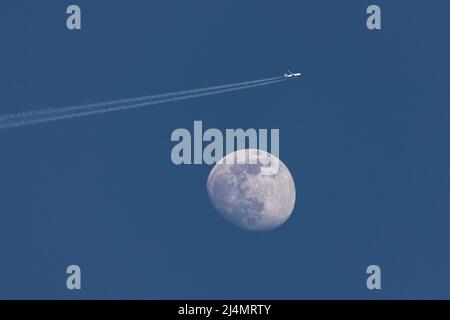 Nahaufnahme des zunehmenden Mondes und eines Flugzeugs, das in der Nähe vorbeifliegt, wodurch eine Aufnahme am frühen Abend gegen den dunkelblauen Himmel hinterlassen wird. Stuttgart, Deutschland Apr Stockfoto