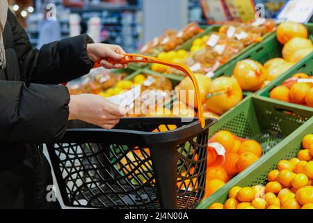 Nahaufnahme einer Frau im Supermarkt, die einen Warenkorb und eine Einkaufsliste auf Papier hält. Stockfoto