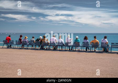 Die Menschen sitzen auf den berühmten blauen Stühlen am Ufer in Nizza - Frankreich und beobachten das azurblaue Wasser des Ligurischen Meeres, die Ruhe, das Alter, die Ruhe, das Alter Stockfoto