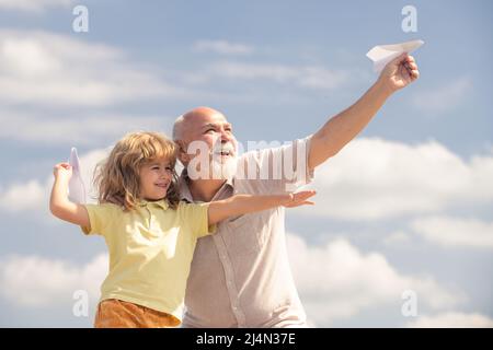 Enkelkind und Großvater mit Spielzeug Papierflugzeug vor Sommerhimmel Hintergrund. Kleiner Junge mit Träumen vom Fliegen. Stockfoto