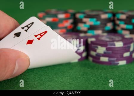 Eine kaukasische Hand hebt die Ecke zweier Spielkarten an und zeigt, dass beide Asse sind. Im Hintergrund sind mehrere Stapel Chips zu sehen. Stockfoto