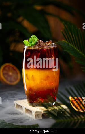 Bumble Kaffee mit Eis auf einem dunklen tropischen Hintergrund. Espresso, Orangensaft und Sirup in Schichten Stockfoto