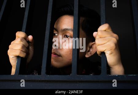 Nahaufnahme Ausdruck von Mann hält Bars im Gefängnis. Sieht traurig und traurig. Konzept der Korruption Stockfoto