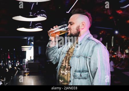 Mann trinkt Bier. Seitenansicht eines hübschen jungen Mannes, der Bier trinkt, während er an der Theke sitzt. Das Konzept der schlechten Gewohnheiten und Alkoholabhängigkeit. Lo Stockfoto