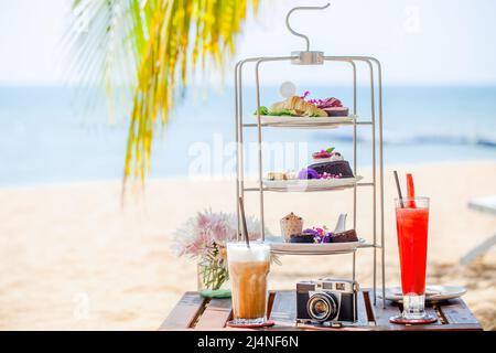 Nachmittagstee am tropischen Sandstrand mit blauem Meer und Palmenblatt im Hintergrund Stockfoto