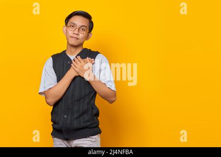 Glück junger asiatischer Mann, der beide Handflächen auf der Brust isoliert auf gelbem Hintergrund hält Stockfoto