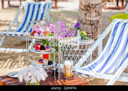 Nachmittagstee am tropischen Sandstrand mit blauem Meer und Palmenblatt im Hintergrund Stockfoto