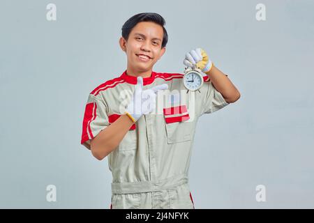 Porträt eines lächelnden, gutaussehenden Mannes mit mechanischer Uniform und Wecker auf grauem Hintergrund Stockfoto