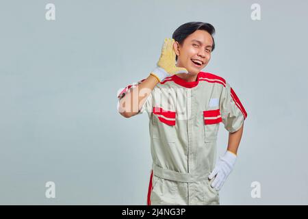 Porträt eines wirklich hübschen Mannes mit mechanischer Uniform, der versucht, ein geheimes Gespräch auf grauem Hintergrund zu hören Stockfoto