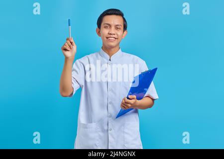 Attraktive junge asiatische männliche Krankenschwester hält Stift und mit guten Idee isoliert über blauen Hintergrund Stockfoto