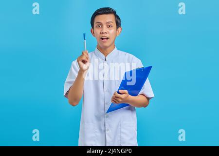Attraktive junge asiatische männliche Krankenschwester hält Stift und mit guten Idee isoliert über blauen Hintergrund Stockfoto