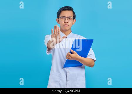 Wütend männlichen Krankenschwester hält Zwischenablage und tun Stop-Geste mit Handflächen auf blauem Hintergrund Stockfoto