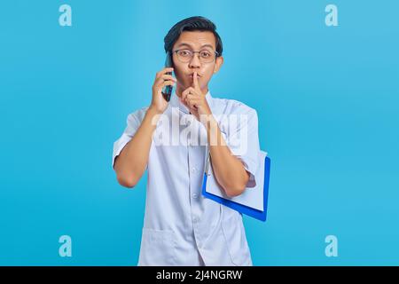 Krankenschwester, die auf einem mobilen Gerät mit Zwischenablage spricht und auf gelbem Hintergrund eine stille Geste macht Stockfoto