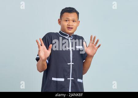 Porträt eines überraschten asiatischen jungen Mannes mit Karate auf grauem Hintergrund Stockfoto