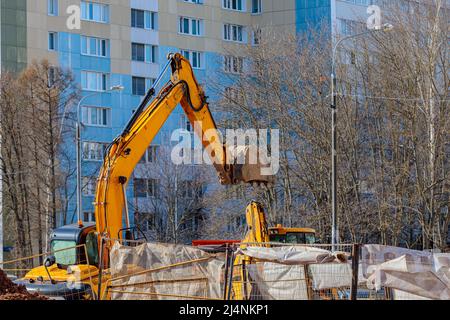 Ein Bagger mit einem großen Eimer gräbt ein Loch im Hof. Stockfoto