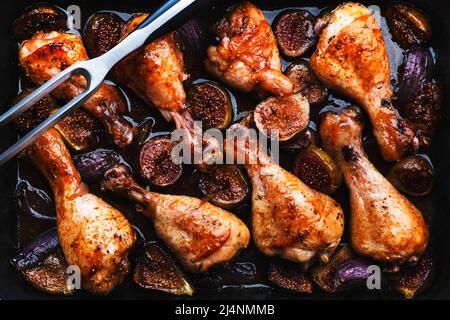 Gebackene Hähnchenbeine, Drumsticks mit süßen Feigen und Zwiebeln in balsamischer Marinade auf schwarzem Backblech, rostiger grüner Tischhintergrund, Draufsicht Stockfoto