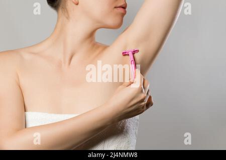 Frau rasieren sich mit dem ergonomischen Rasierer in Pink sanft zur Achselhöhlen-Epilation. Körperpflege Hautpflege Beauty-Konzept Stockfoto
