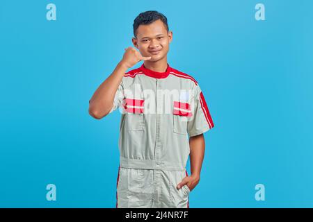 Porträt eines lächelnden jungen asiatischen Mechanikers, der auf blauem Hintergrund ein Rufzeichen macht Stockfoto