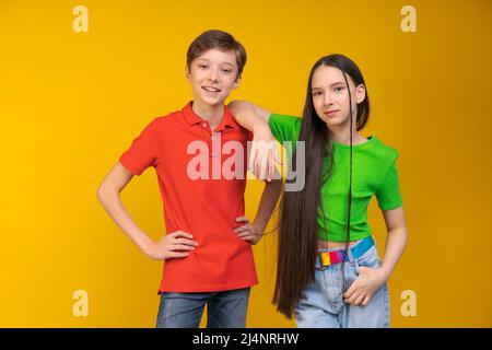 Kerl und Mädchen in hellen T-Shirts auf gelbem Hintergrund Mädchen legte ihre Hand auf die Schulter des Mannes. Nette Teenager schauen auf die Kamera. Jugendfreundschafts- und Unterstützungskonzept Stockfoto