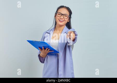 Portrait der schönen jungen asiatischen Geschäftsfrau in Anzug stehend halten Dokument Ordner und zeigen mit Stift isoliert auf lila Hintergrund Stockfoto