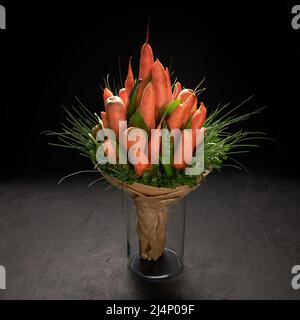 Bouquet von reifen Karotten, grünem Pfeffer und Petersilie steht in einer Vase auf schwarzem Hintergrund Stockfoto