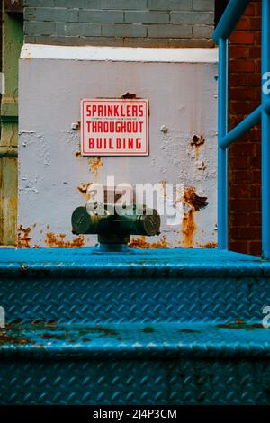 Grüne Sprinklerrohrleitung in Manhattan auf blauen Metalltreppen mit Schild mit der Aufschrift: „Sprinkler im gesamten Gebäude“ Stockfoto