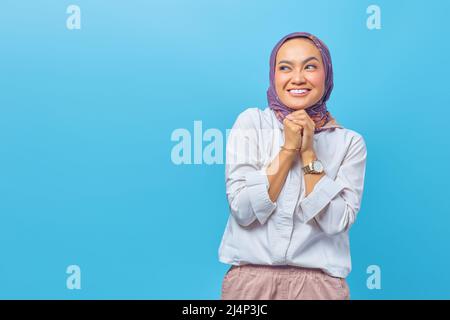 Porträt einer glücklichen jungen asiatischen Frau, die fröhlich neben der Seite mit zusammenklappbarer erhobener Hand schaut Stockfoto