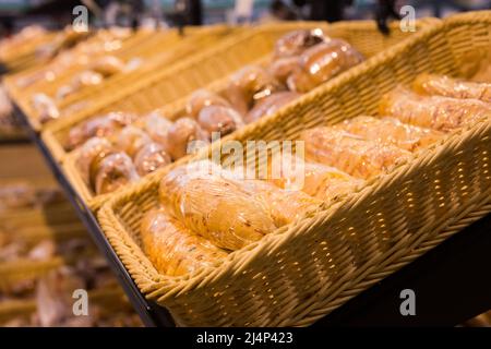 Frische goldene Brote mit geschmolzenem Käse in Plastikfolie in Korbkorb in der Brotabteilung des Supermarkts eingewickelt Stockfoto