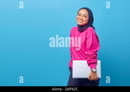 Porträt eines schönen lächelnden asiatischen muslimischen College-Studenten in rosa Pullover mit Laptop Stockfoto