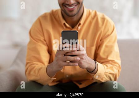 Lächelnder junger Mann mit Smartphone zu Hause, Nahaufnahme Stockfoto
