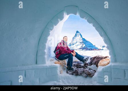 Porträt eines Mannes, der sich am Eingang des Igloos gegen das Matterhorn im Hintergrund entspannt Stockfoto