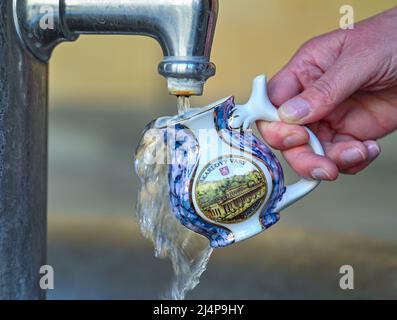 11. April 2022, Tschechische Republik, Karlovy Vary: Eine Frau holt Wasser aus einer heißen Quelle im Zentrum von Karlovy Vary (Tschechisch: Karlovy Vary) mit einem original Karlsbader Schnabelbecher. Karlovy Vary ist eine Kurstadt in der Region Böhmen im westlichen Teil der Tschechischen Republik. Dank seiner zahlreichen Thermalquellen ist die Stadt am Rande des Erzgebirges seit dem 19.. Jahrhundert ein beliebtes Touristenziel. Foto: Patrick Pleul/dpa Stockfoto