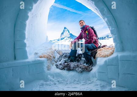 Tourist sitzt am Eingang des Igloos gegen das Matterhorn im Hintergrund Stockfoto