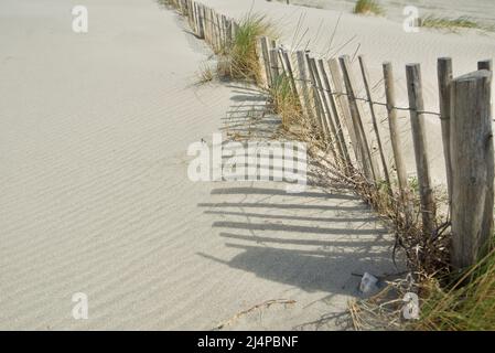 Holzzaun, der Sanddünen an einem Strand entlang der Küste schützt, ein Holzpfeilzaun. Seeverteidigung verhindert Erosion. Schöne Kunst Stockfoto