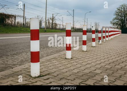 Metallstangen befinden sich am Rand des Gehwegs. Diese sind mit roten und weißen Streifen bemalt. Stockfoto