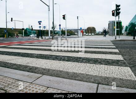 Fußgängerübergang, der durch eine Ampel gesteuert wird. Roter Fahrradteppich mit weißen Streifen. Stockfoto